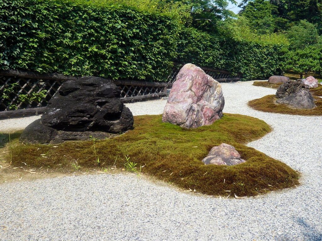 Japanischer Zen-Garten mit Findlingen auf Moosinseln in einer geharkten Kiesfläche